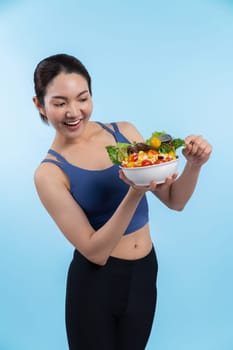 Young sporty Asian woman in sportswear holding salad bowl fill with vibrant of fruit and vegetable. Natural youthful and fit body lifestyle with balance nutrition on isolated background. Vigorous