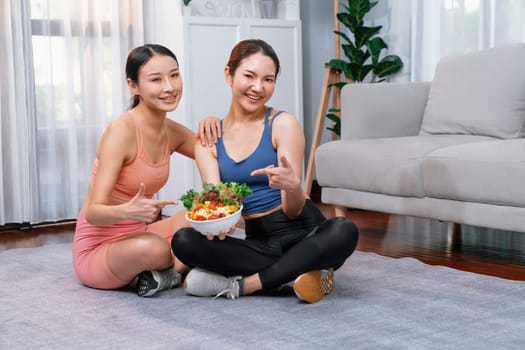 Young sporty Asian women in sportswear holding salad bowl together fill with vibrant of fruit and vegetable. Natural youthful and fit body lifestyle with balance nutrition and home exercise. Vigorous