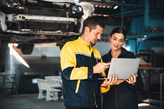 Two vehicle mechanic working together, conduct car inspection with laptop. Automotive service technician in uniform carefully make diagnostic troubleshooting to identify error. oxus