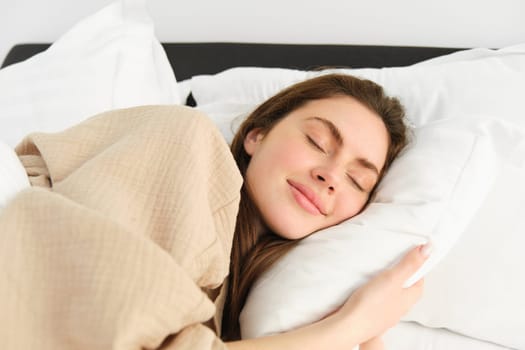 Portrait of smiling brunette woman in pyjamas, sleeping in hotel bed, relaxing with pleased face, dreaming, sleeping in bedroom.