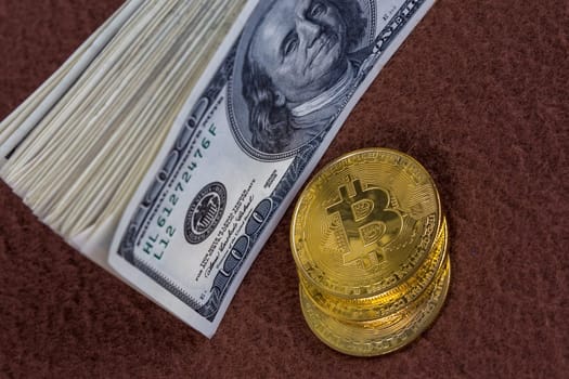 a bunch of us dollar banknotes and three bitcoin shiners on brown fleece background close-up with selective focus