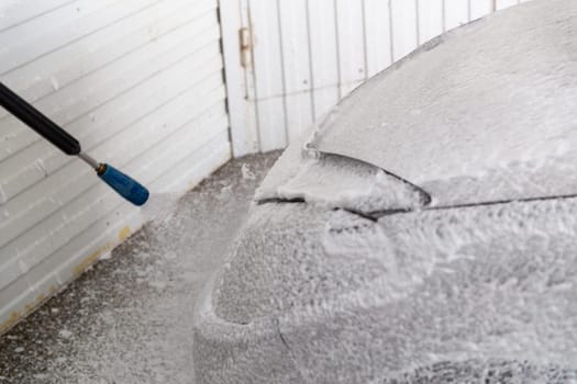 process of applying white pressurized non-contact foam to a car from gun for car wash.