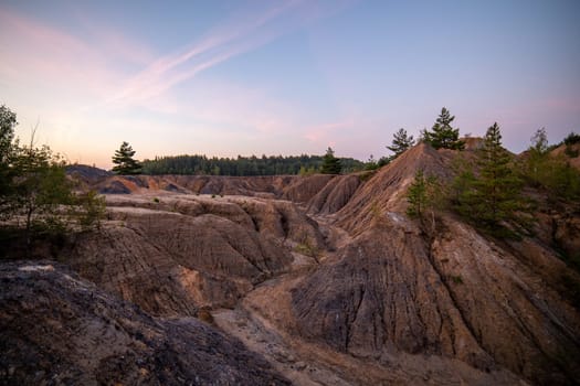 eroded soil quarry ravine with forest on its edge at summer evening.