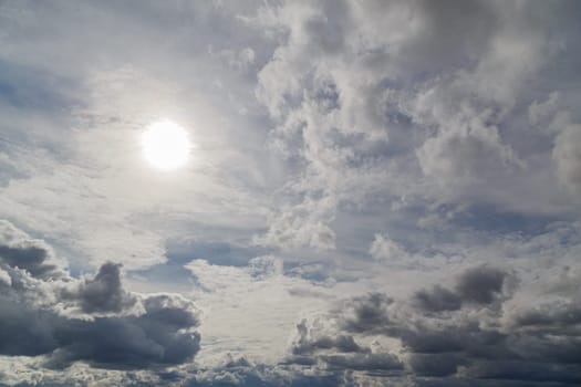 blue sky with sun and mixed clouds on different layers, above horizon view.