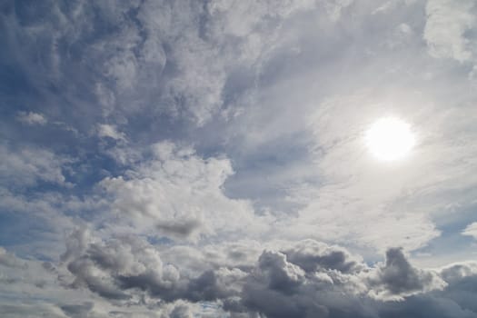 blue sky with sun and mixed clouds on different layers, above horizon view.