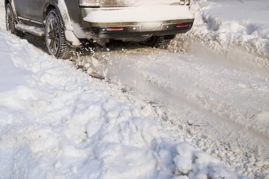 Road snow flies up from a vehicle's spinning wheel. Car's wheels spin and spew up pieces of snow it attempts to gain traction on the slippery road at winter daytime.