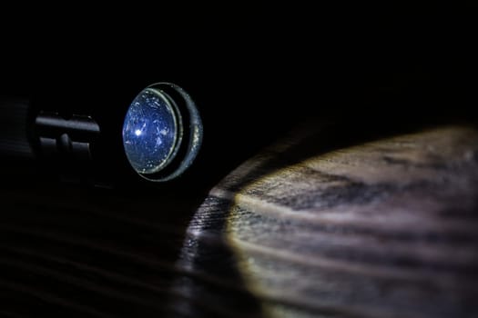Black led operational flashlight on rough wooden surface - closeup with selective focus.