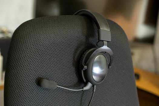black headset on backrest of empty computer chair with air mesh upholstery.