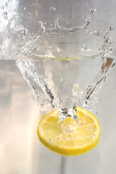 Lemon slice falls into glass of water