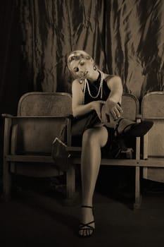 A woman dressed in the style of the 20s sits in the cinema with her foot outstretched