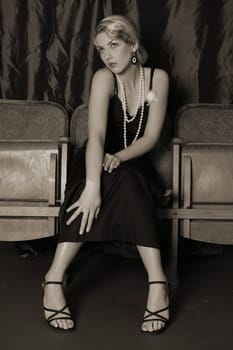 A woman dressed in the style of the 20s sits intently in the cinema with her hands on her knees