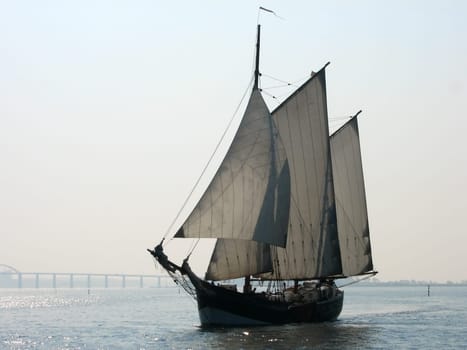 The fog laid a gray veil over the Baltic Sea. The sun tried with all its might to drive away the fog. The sailor sails through the fairway at Rudkøbing. In the background the bridge at Rudkøbing,which connects the islands of Langeland with Tåsinge.