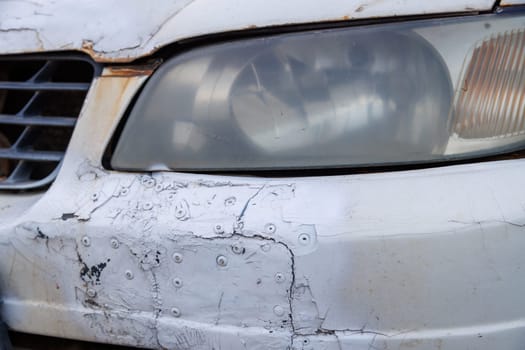 old white car bumper neglectly fixed with patches and rivetts and painted over with can of spraypaint, closeup view.