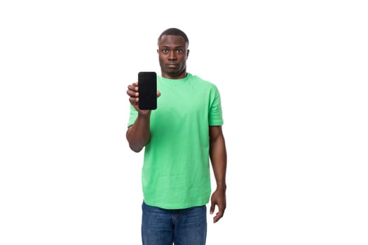 a young american guy dressed in a mint t-shirt holds a smartphone with the screen facing forward.