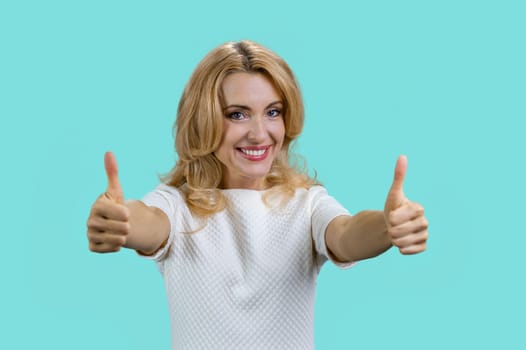 Portrait of a smiling blond woman gives both thumbs up. Isolated on turquoise.