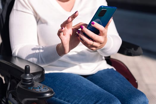 unrecognizable woman using wheelchair using mobile phone, concept of technology of communication and mobility