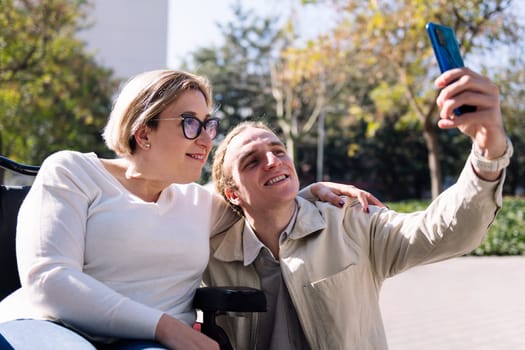 smiling couple of a man and woman using wheelchair taking a selfie photo with mobile phone, concept of friendship and technology of communication
