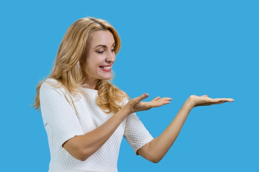 Mature caucasian woman presenting copy space with both hands. Isolated on blue.