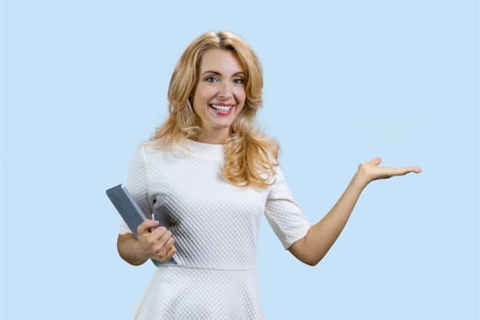 Portrait of a mature happy caucasian woman holding a tablet device and showing copy space. Isolated on pale blue.