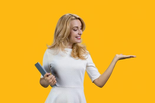 Happy caucasian woman holding a tablet device and showing copy space. Isolated on vivid yellow.