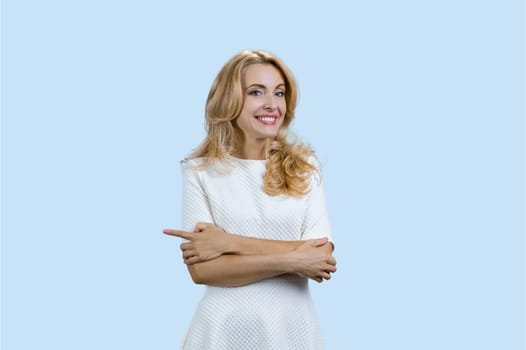 Portrait of happy cheerful blonde woman with folded arms pointing to the right. Isolated on turquoise.