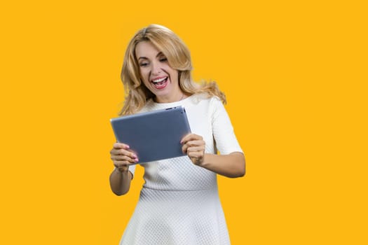 Portrait of happy mature lady plays video game on the tablet device. Isolated on yellow.