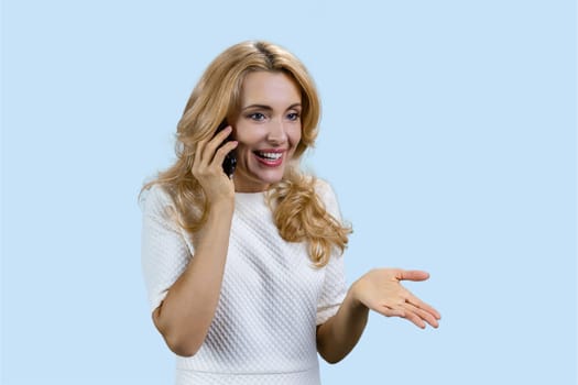 Portrait of happy mature blonde talking on the phone. Isolated pastel blue background.
