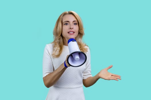 Attractive blonde woman giving a speech in megaphone on colorful background. Isolated on turquoise.