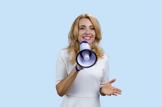 Mature blonde woman giving a speech in loudspeaker on colorful background. Isolated on pale blue.