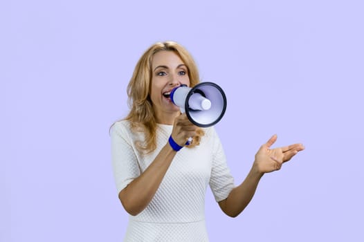 Happy positive blonde woman giving a speech in megaphone. Isolated on purple.