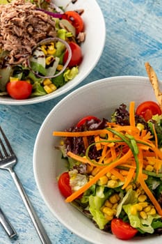 Salad with tuna, carrots, tomatoes, corn and plenty of greens on white porcelain plates