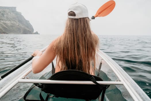 Woman in kayak back view. Happy young woman with long hair floating in transparent kayak on the crystal clear sea. Summer holiday vacation and cheerful female people having fun on the boat.