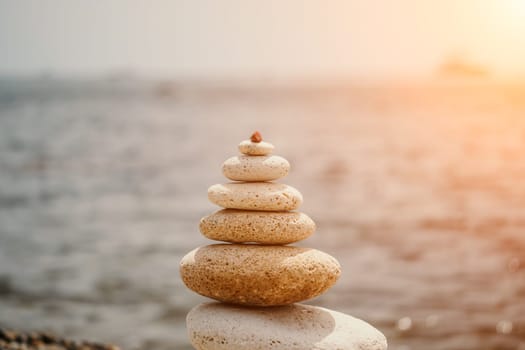 Pyramid stones on the seashore with warm sunset on the sea background. Happy holidays. Pebble beach, calm sea, travel destination. Concept of happy vacation on the sea, meditation, spa, calmness.