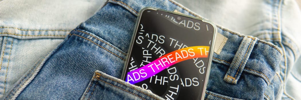 Tver, Russia - July 15, 2023, the threads logo on the smartphone screen lying on the jeans. The threads icon. The logo of the current application. Threads social network