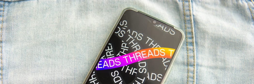 Tver, Russia - July 15, 2023, the threads logo on the smartphone screen lying on the jeans. The threads icon. The logo of the current application. Threads social network