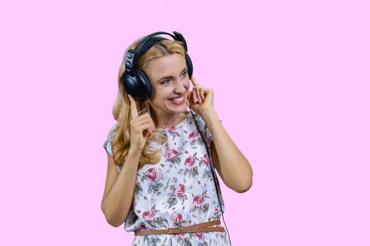 Blonde woman listening to music in headphones. Isolated on pink.