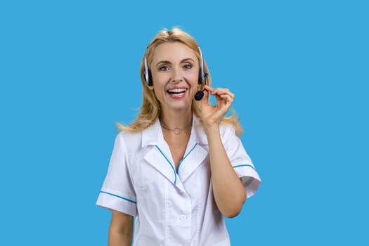 Portrait of blonde mature female doctor wearing headset. Isolated on blue.