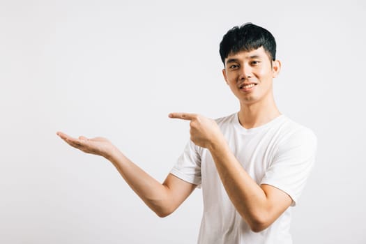 Portrait of a smiling, happy man pointing his finger to the side with confidence. Asian young man in a studio shot isolated on white, providing copy space.