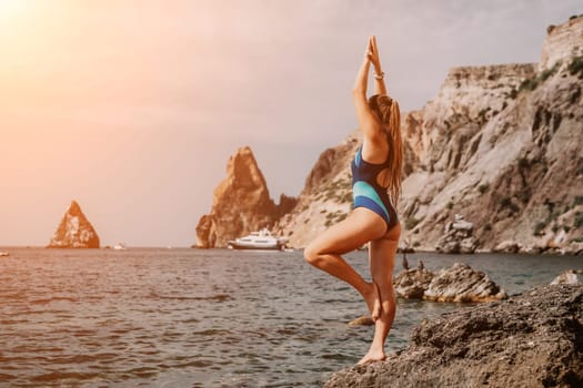 Woman sea yoga. Back view of free calm happy satisfied woman with long hair standing on top rock with yoga position against of sky by the sea. Healthy lifestyle outdoors in nature, fitness concept.