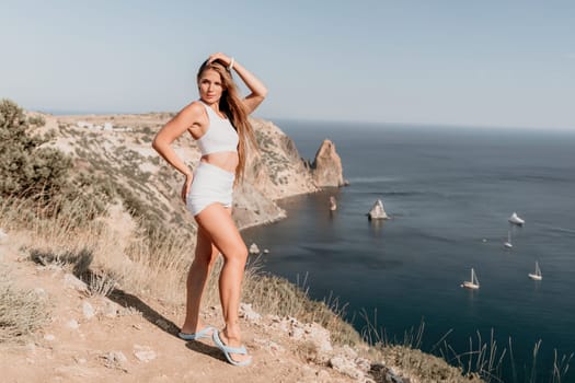 Woman travel sea. Young Happy woman in a long red dress posing on a beach near the sea on background of volcanic rocks, like in Iceland, sharing travel adventure journey