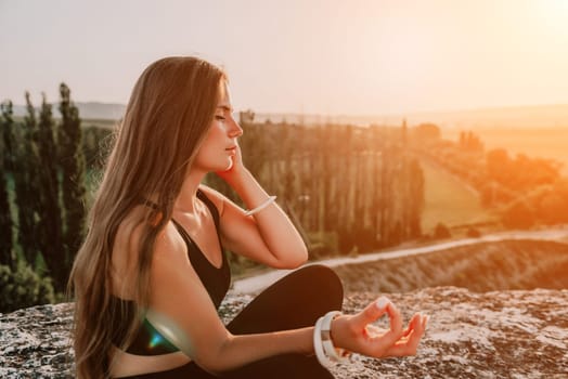 Well looking middle aged woman with long hair, fitness instructor in leggings and tops doing stretching and pilates on the rock near forest. Female fitness yoga routine concept. Healthy lifestyle.