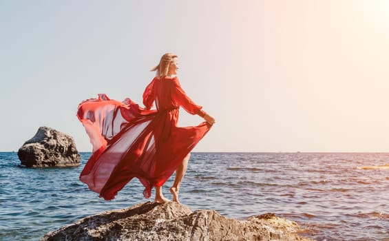 Woman travel sea. Young Happy woman in a long red dress posing on a beach near the sea on background of volcanic rocks, like in Iceland, sharing travel adventure journey