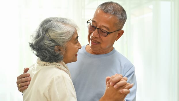 Romantic senior couple dancing in living room, enjoying free time together at home.