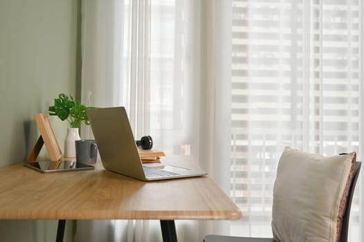 Comfortable home interior with laptop computer, books and potted plant on wooden table.