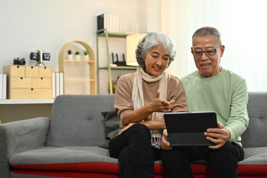 Happy senior couple using digital tablet scrolling, reading news feed in social media and browsing internet.