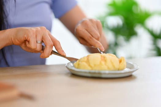 Cropped shot of young woman eating homemade eating a big cream puff. People, food and lifestyle concept.