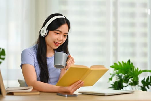 Attractive young woman in headphone reading book at home. Education, leisure and lifestyle concept.