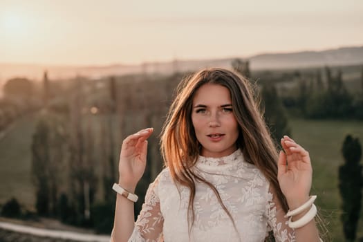 Romantic beautiful bride in white dress posing with sea and mountains in background. Stylish bride standing back on beautiful landscape of sea and mountains on sunset