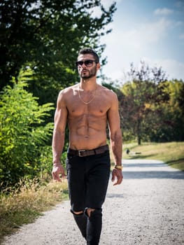 A shirtless man walking down a dirt road. Photo of a shirtless athletic fit man walking down a dirt road