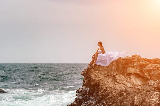 Woman sea white dress. A woman in a storm sits on a stone in the sea. Dressed in a white long dress, waves crash against the rocks and white spray rises